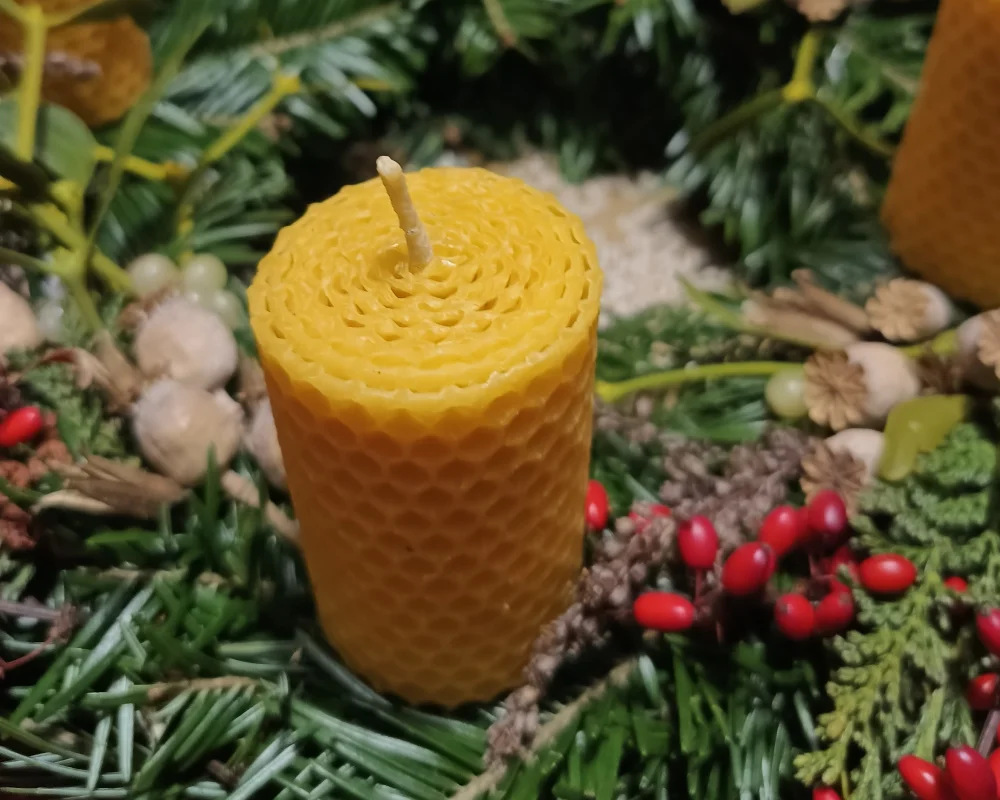 Detail motané svíčky z včelího vosku zasazené v adventním věnci s chvojím a červenými bobulemi